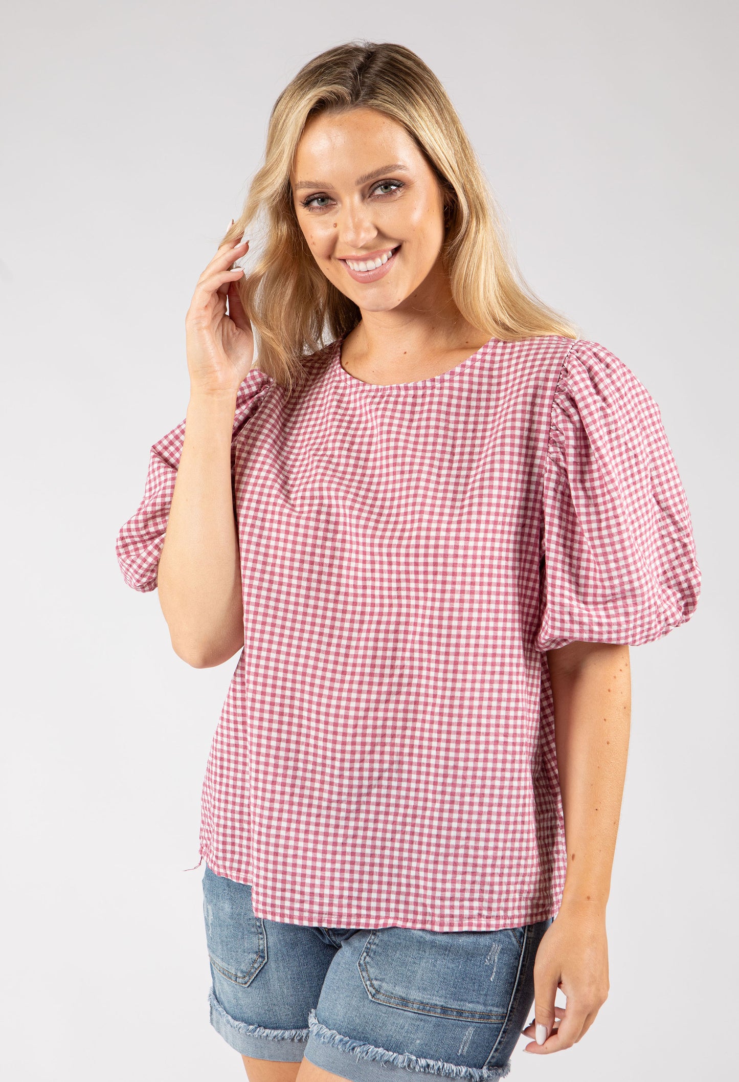 Woman wearing a red and white checkered blouse with puffed sleeves on a plain background