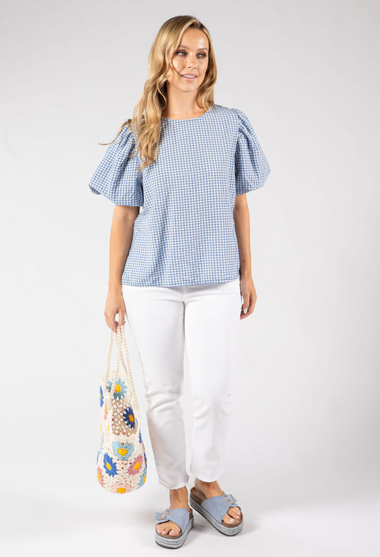 Woman wearing a blue checkered top and white pants, holding a floral bag on a white background