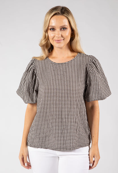 Woman wearing a brown and white checkered blouse against a plain background