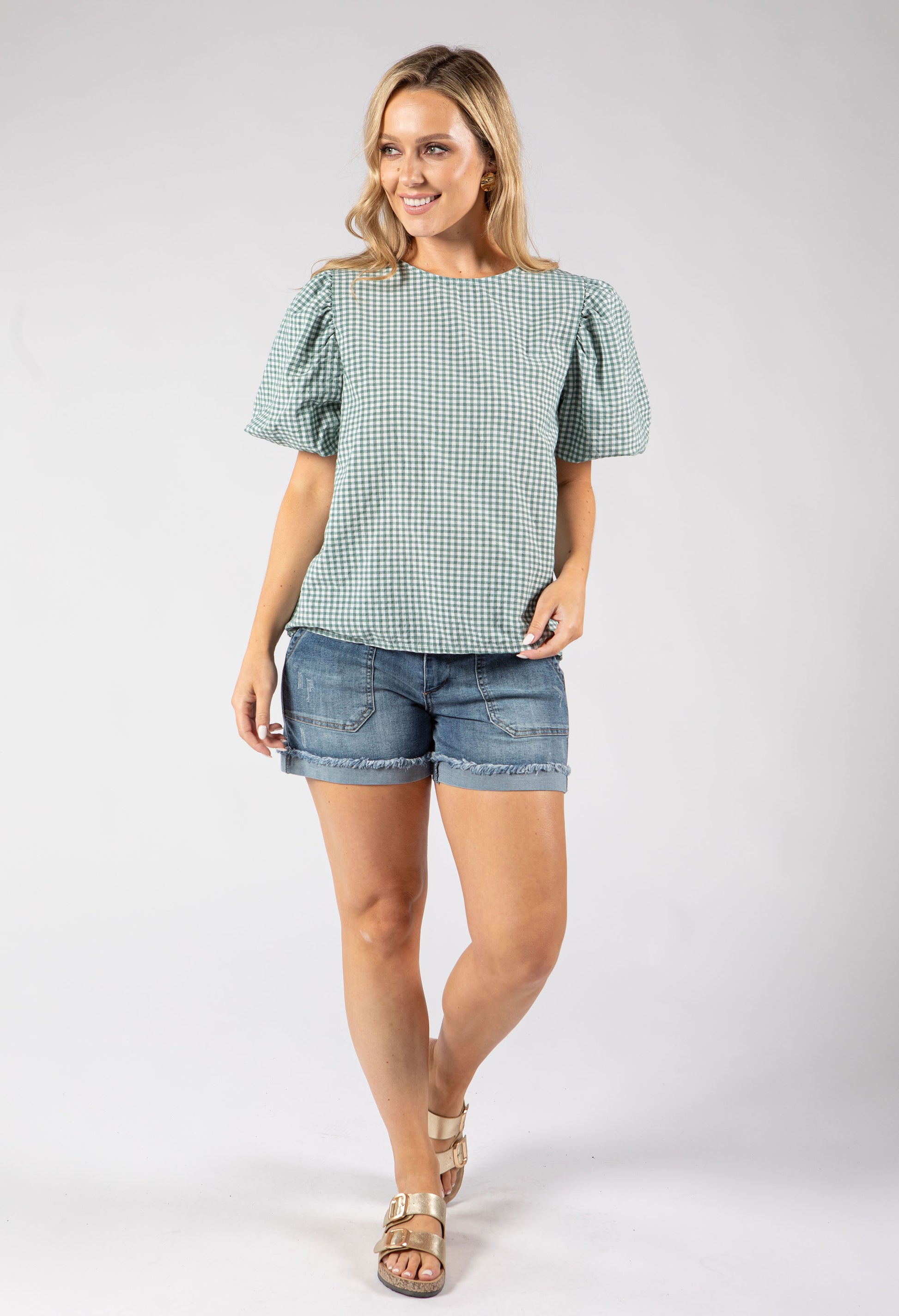 Woman wearing a green checkered top and denim shorts on a white background
