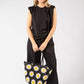 Woman holding a black tote bag with white daisy patterns against a white background
