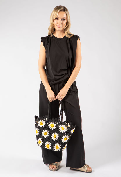 Woman holding a black tote bag with white daisy patterns against a white background