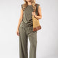 Woman wearing a green jumpsuit holding a brown bag on a white background