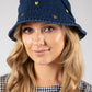 Woman wearing a blue denim bucket hat with gold buttons on a gray background