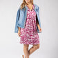 Woman wearing a pink leaf-patterned dress with a denim jacket on a white background