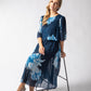 Woman wearing a blue floral dress standing next to a black stool on a white background