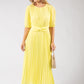 Woman wearing a yellow pleated dress holding a beige handbag on a white background