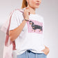 Woman wearing a white t-shirt with a dachshund graphic and a pink jacket on a gray background