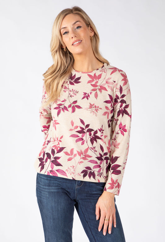 A woman modeling a long-sleeve crewneck top with a pink, magenta, and burgundy floral pattern on a light beige background.