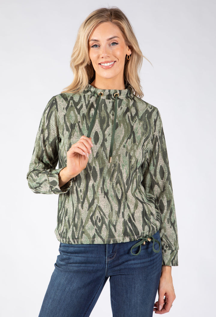 A woman modeling a sage green and olive green abstract patterned long-sleeve top with a drawstring waistband.