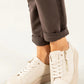 A close-up of a person wearing off-white leather platform sneakers with side zippers and laces, paired with dark brown cuffed pants against a clean white background.