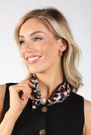 A smiling blonde woman wearing a black sleeveless top and a pink, black, and white leopard-print neck scarf with a pearl accent, set against a plain light gray background.