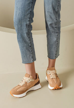 A person wearing light blue cropped jeans and tan-and-white athletic sneakers, standing in a clean beige indoor setting.