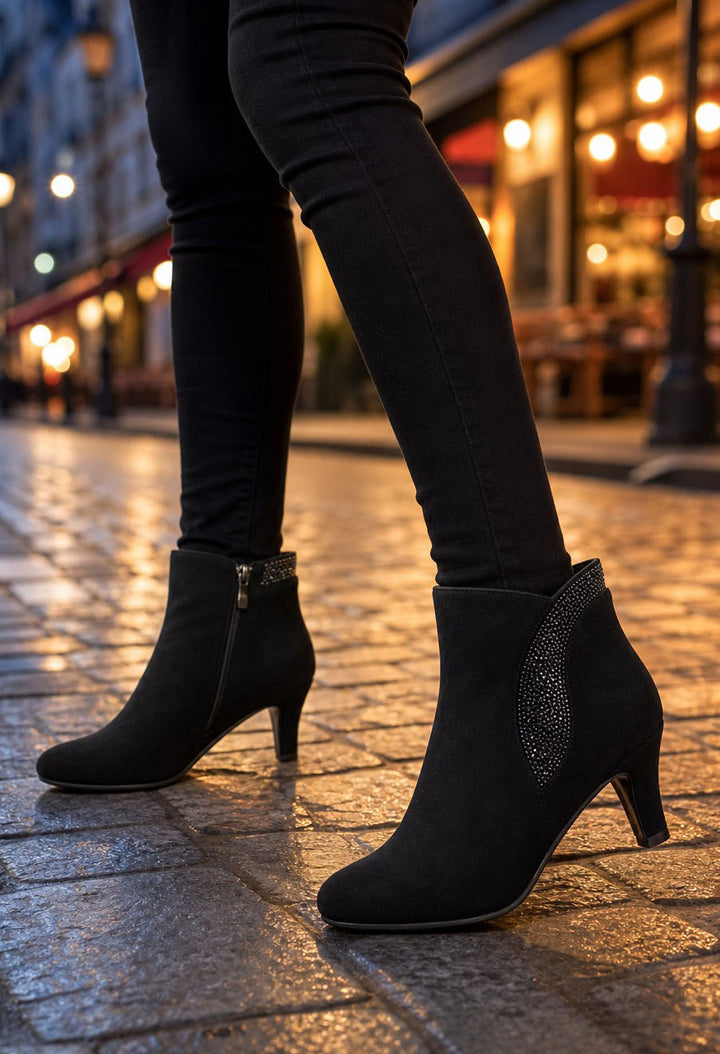 Black ankle boots with kitten heels and side embellishments, worn with black skinny jeans on a cobblestone street at night.