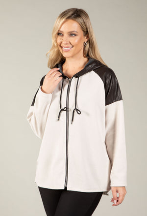 A woman modeling a color-blocked zip-up hoodie with an off-white body and black faux-leather shoulder and hood details, set against a plain light gray studio background.