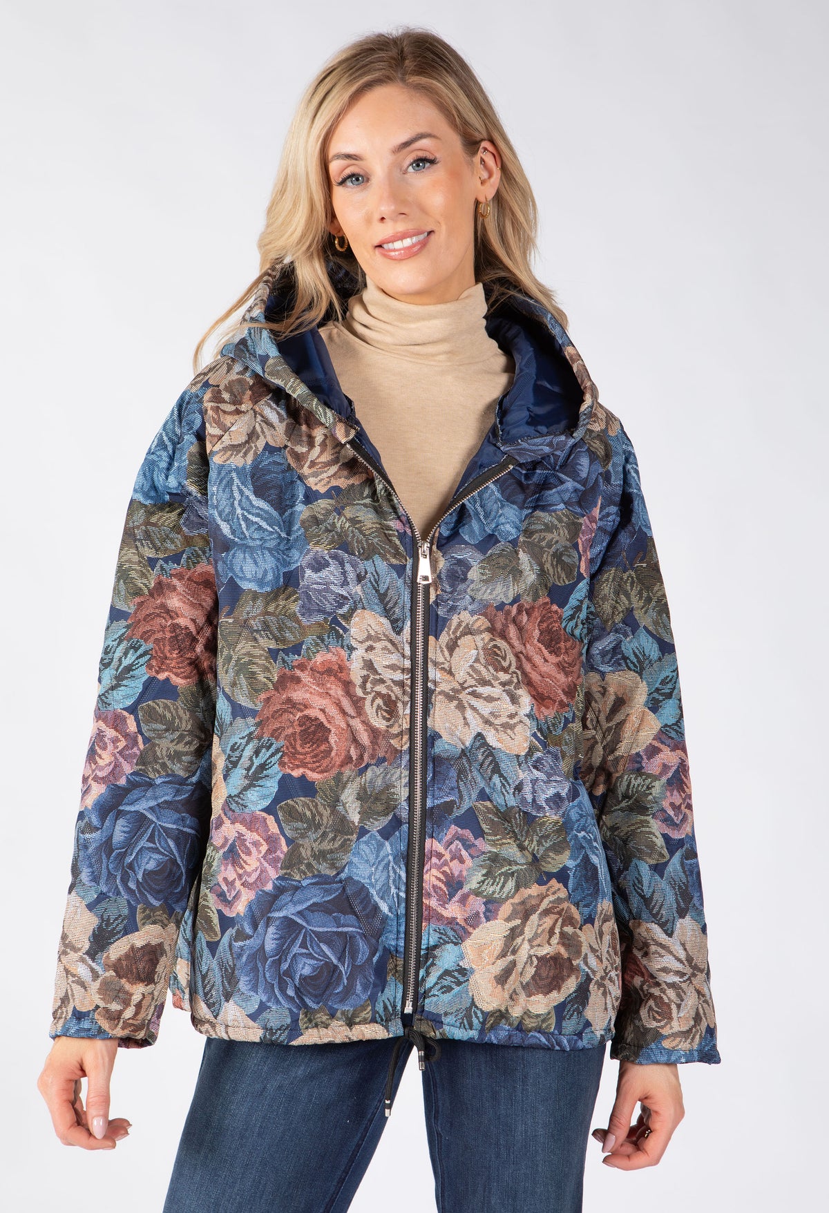 Model wearing a hooded zip-up jacket, small front pockets, and with a large floral print in blue, pink, and beige tones.