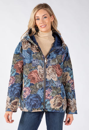 Model wearing a hooded zip-up jacket, small front pockets, and with a large floral print in blue, pink, and beige tones.