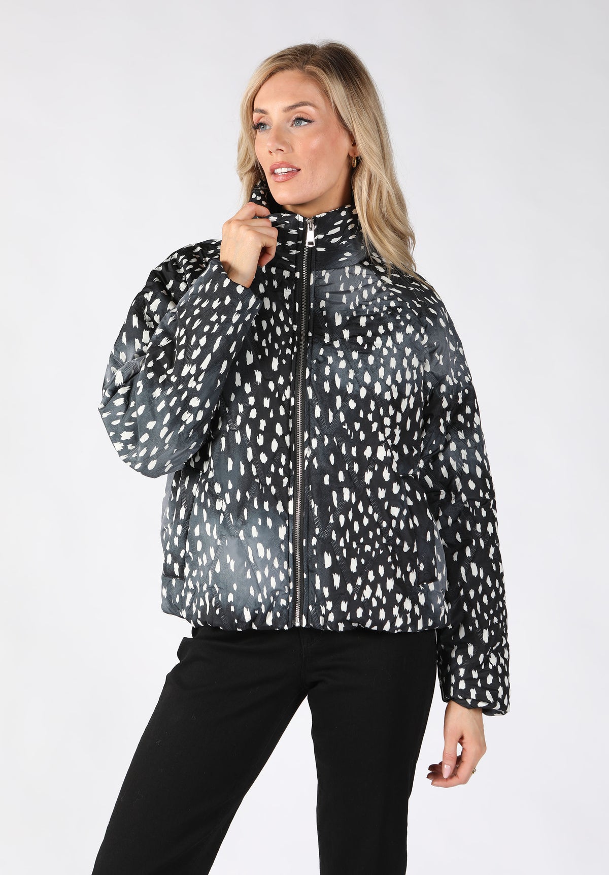 A woman modeling a black and white spotted patterned puffer jacket with a high collar and front zipper.