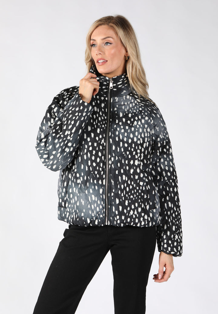 A woman modeling a black and white spotted patterned puffer jacket with a high collar and front zipper.