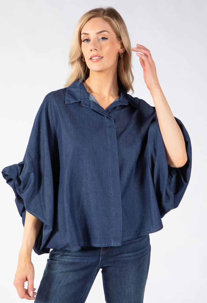 A woman modeling a dark blue, loose-fitting button-up blouse with wide and draped sleeves.
