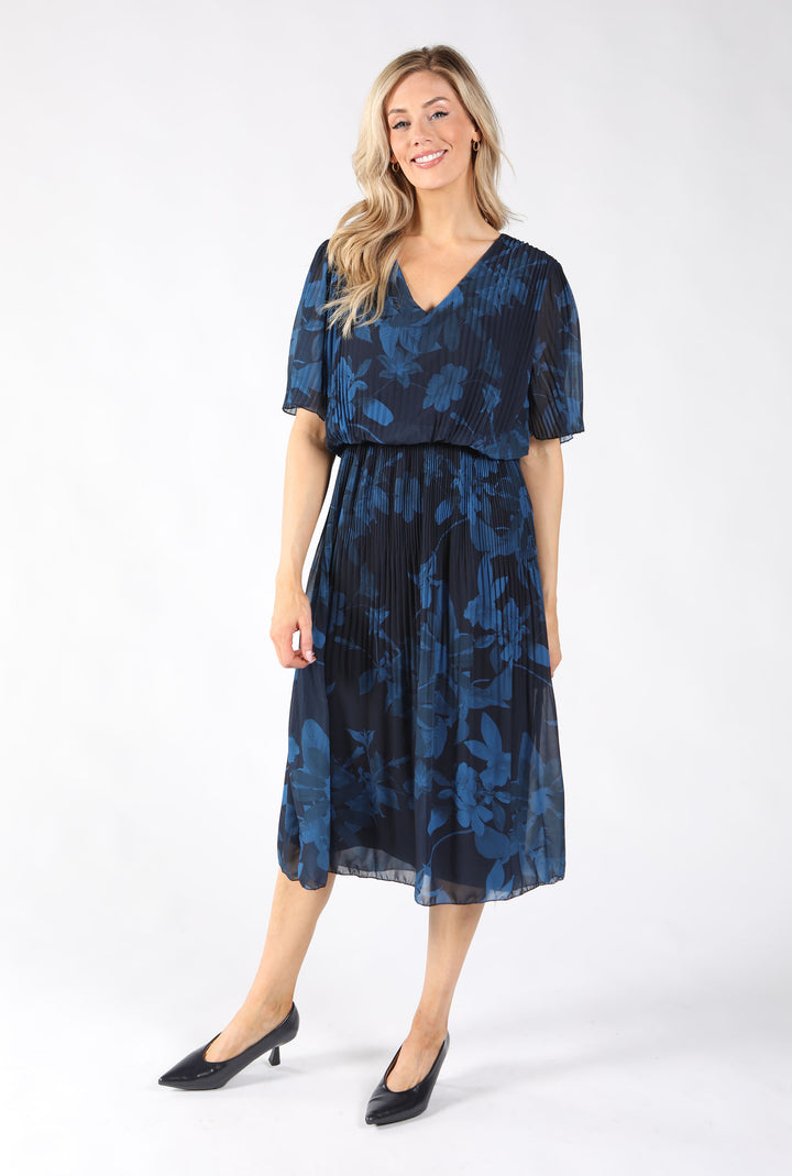 A woman modeling a navy blue midi dress with a dark blue floral pattern, featuring short flutter sleeves, a V-neckline, and a pleated skirt.