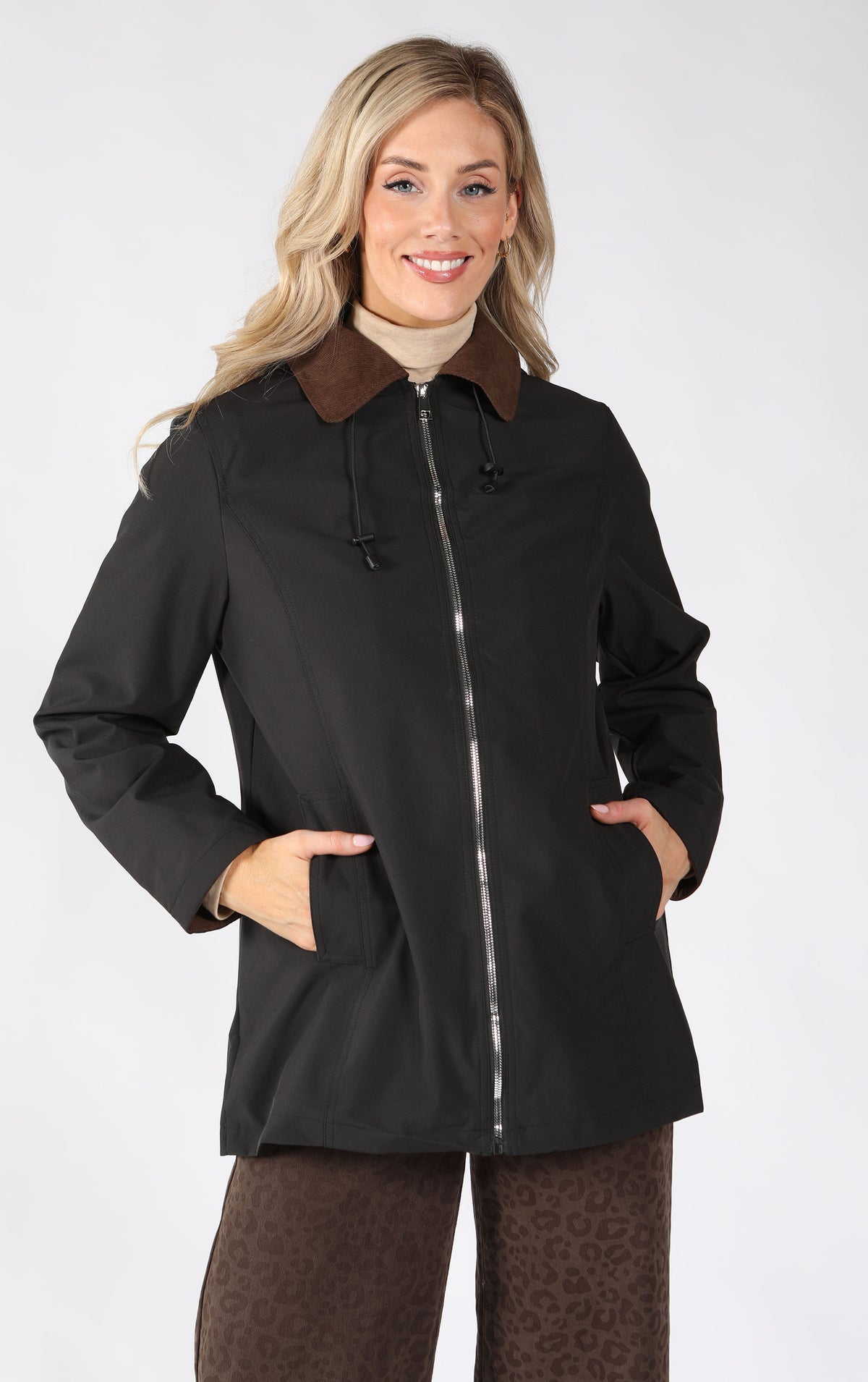A woman modeling a black hooded jacket with a brown collar, front zipper, and side pockets.
