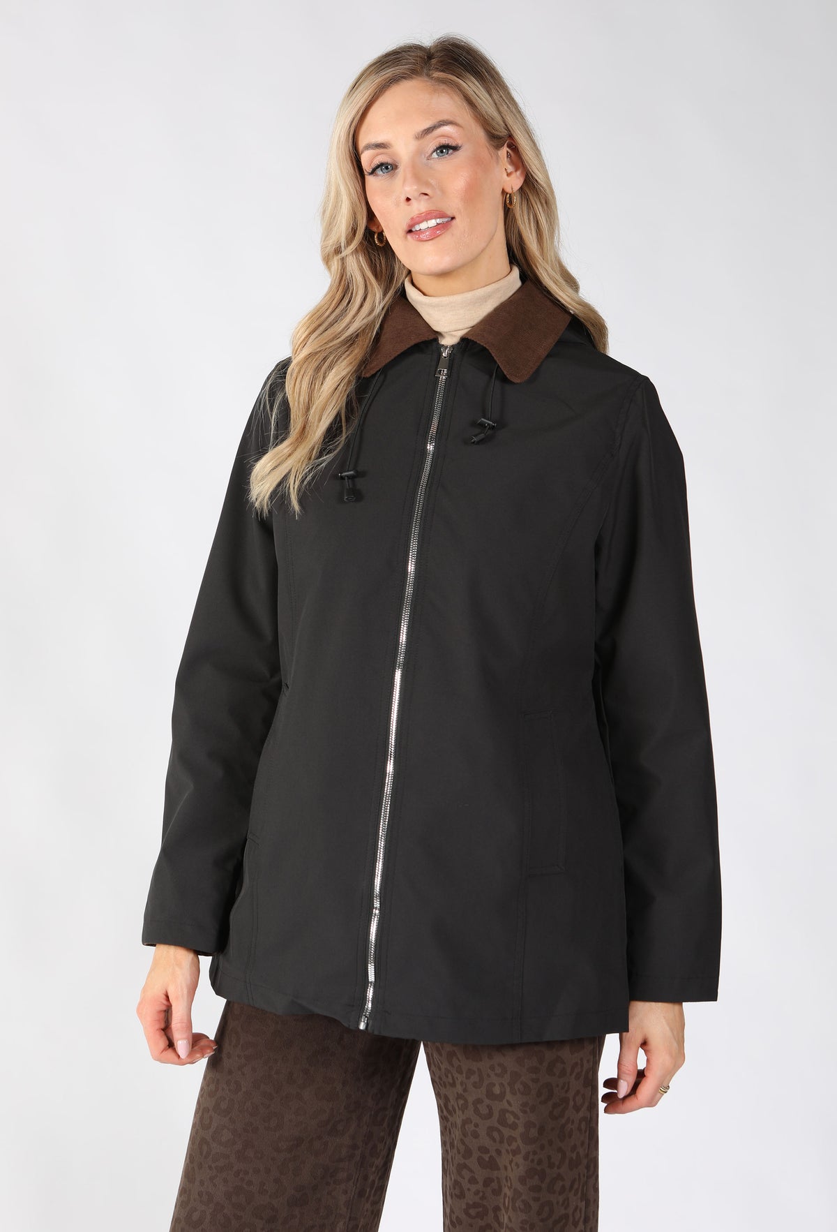 A woman modeling a black hooded jacket with a brown collar, featuring a silver zipper and front pockets.