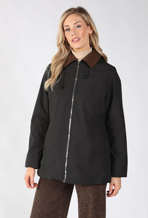 A woman modeling a black hooded jacket with a brown collar, featuring a silver zipper and front pockets.