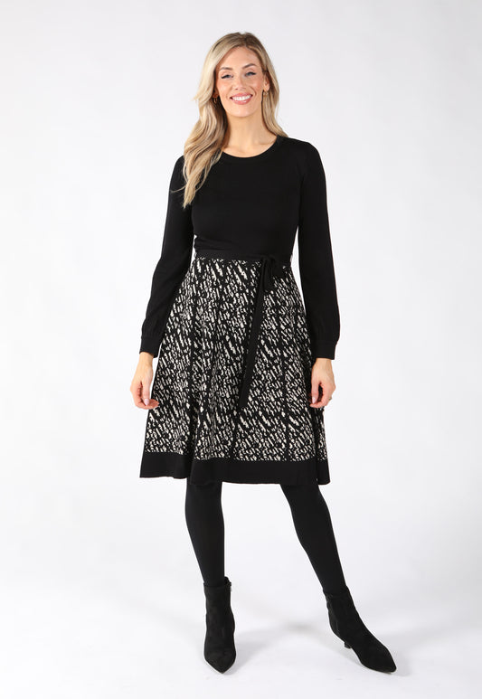Model wearing knitted dress with long sleeves and a standout zig-zag patterned skirt in ivory and black. Cinched with a belt tie.