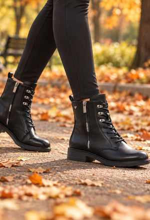 Black lace-up ankle boots with side zippers and silver-tone hardware, worn with black leggings on a path covered in fallen autumn leaves.