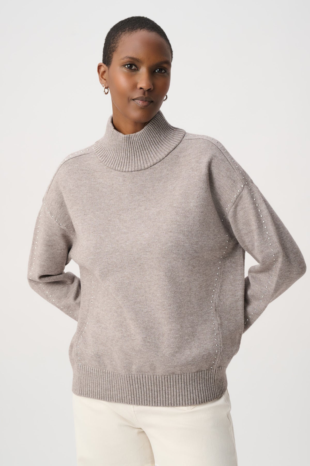 A woman wearing a mauve knit mock neck sweater with subtle silver bead detailing on the shoulders.