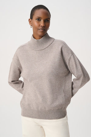 A woman wearing a mauve knit mock neck sweater with subtle silver bead detailing on the shoulders.