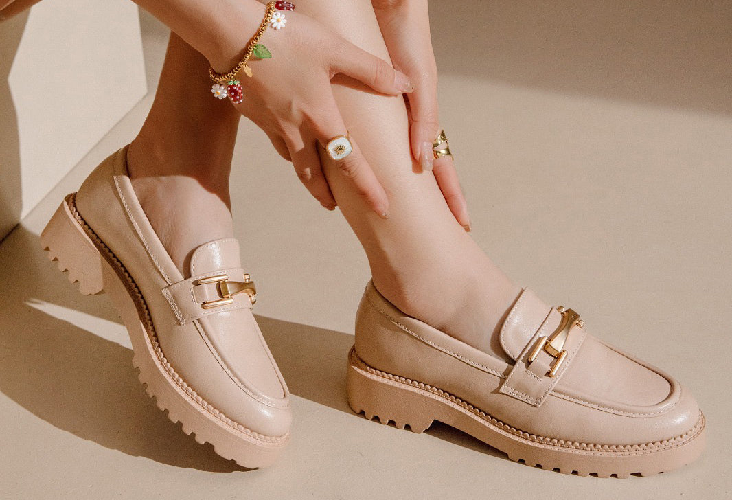 Beige loafers worn by a person on a beige background