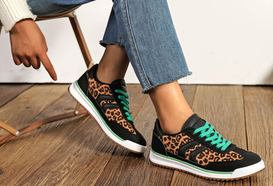 Green and yellow sneakers worn with blue jeans on a wooden floor.