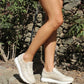 Person wearing light-colored sneakers on a stone path with greenery in the background