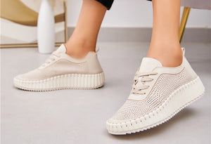 A pair of beige lace-up volume sole trainers with laser cut details, worn with denim jeans.