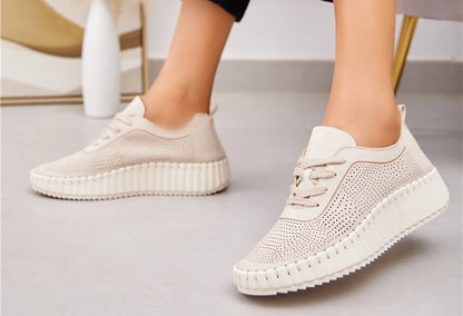 A pair of beige lace-up volume sole trainers with laser cut details, worn with denim jeans.