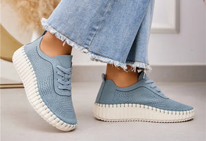 A pair of blue lace-up volume sole trainers with laser cut details, worn with denim jeans.