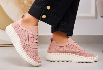 A pair of pink lace-up volume sole trainers with laser cut details, worn with denim jeans.