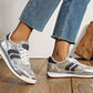 Silver sneakers with blue stripes worn by a person on a wooden floor.