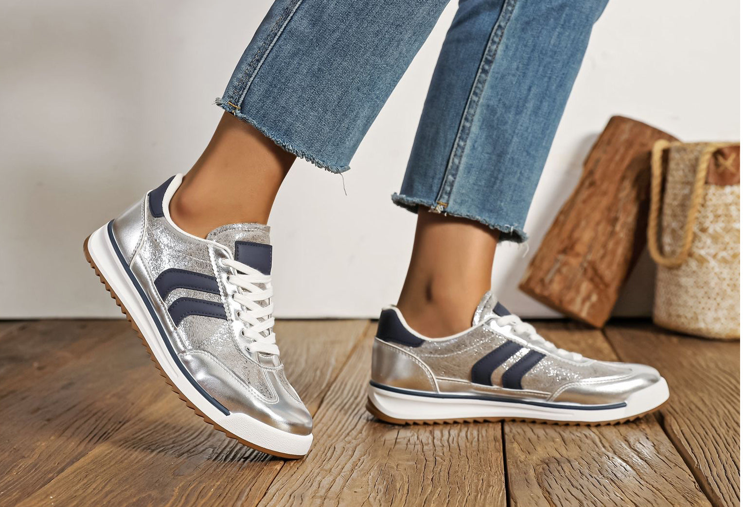 Silver sneakers with blue stripes worn by a person on a wooden floor.