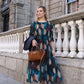 Woman wearing patterned dress holding a navy jacket and camel bag