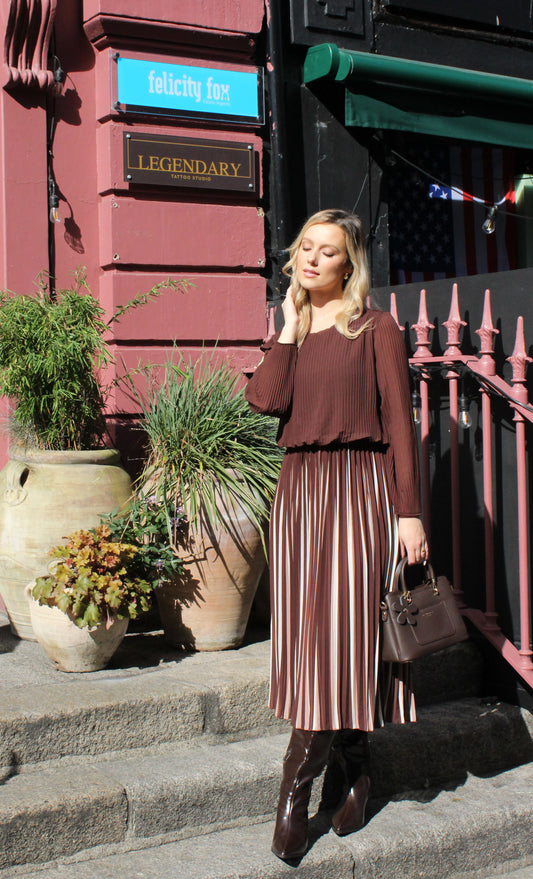 Woman wearing a burgundy top and striped skirt holding a matching handbag on a beige background