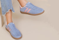 Blue sneakers with pink accents worn by a person on a beige background