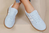 Light blue sneakers with brown soles and white stripes worn by a person on a beige background