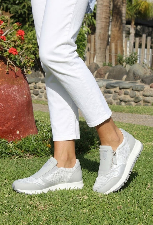 Person wearing light-colored sneakers on a stone path with greenery in the background