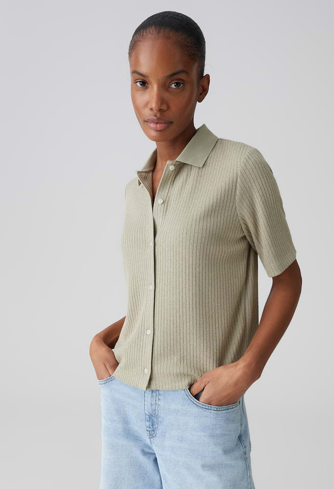 Woman wearing a light green button-up shirt and light blue jeans against a plain background