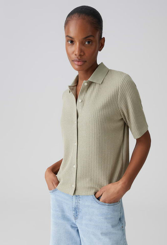 Woman wearing a light green button-up shirt and light blue jeans against a plain background