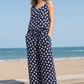 Woman wearing a navy blue jumpsuit with white polka dots by the beach.