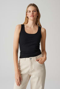 Woman wearing a black tank top and light-colored pants against a plain background